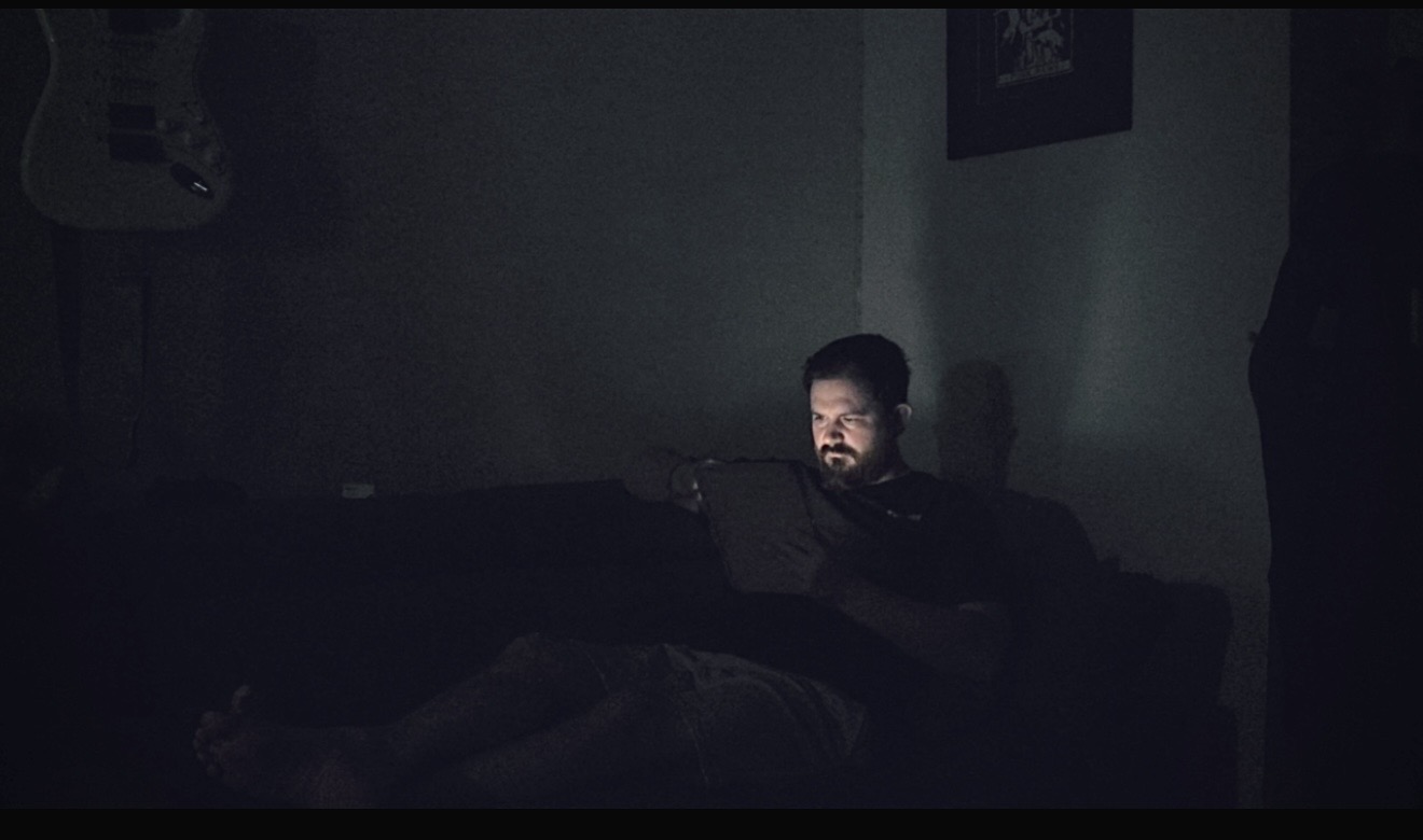 A dimly lit figure sitting on a sofa in a dark room